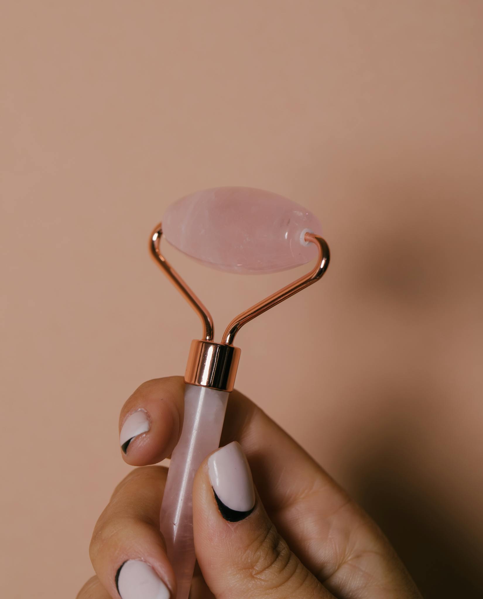 A detailed close-up of a hand holding a facial jade roller with manicured nails against a neutral background.