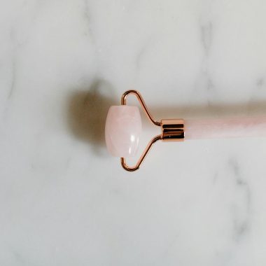 A rose quartz facial roller elegantly placed on a marble surface, emphasizing luxury and skincare.