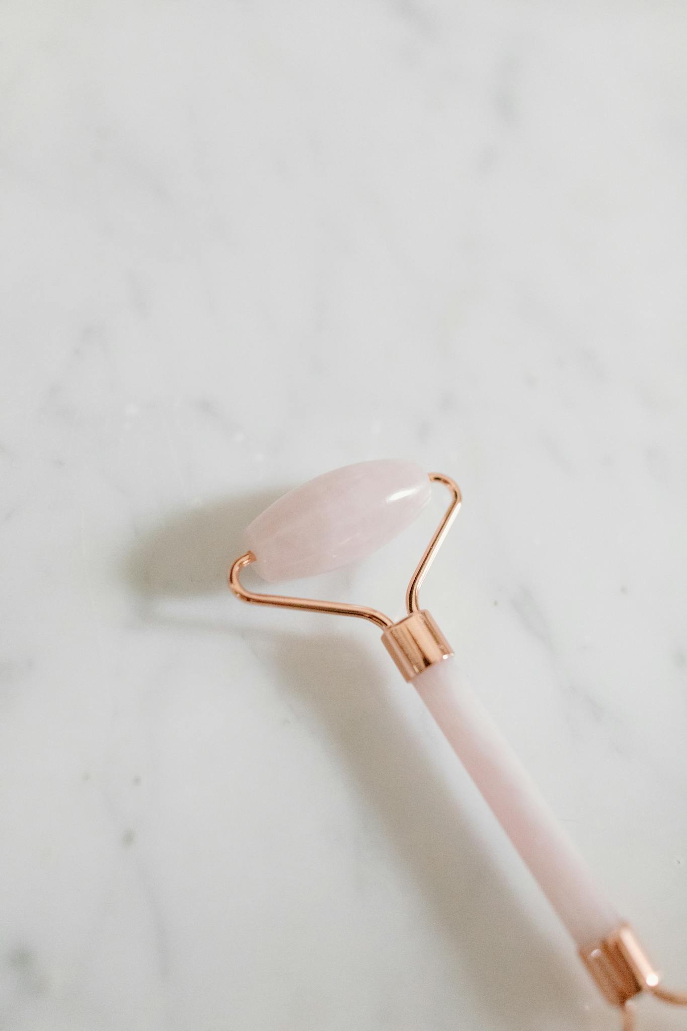 A rose quartz facial roller on a marble surface, symbolizing self-care and beauty routine.