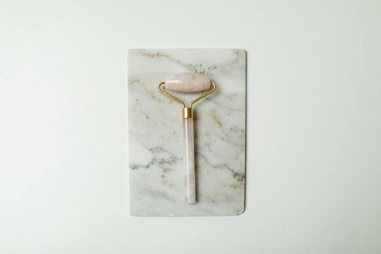 A rose quartz facial roller on a marble slab, perfect for skincare routines.