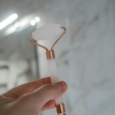 Close-up of a hand holding a rose quartz facial roller, ideal for skincare routines.