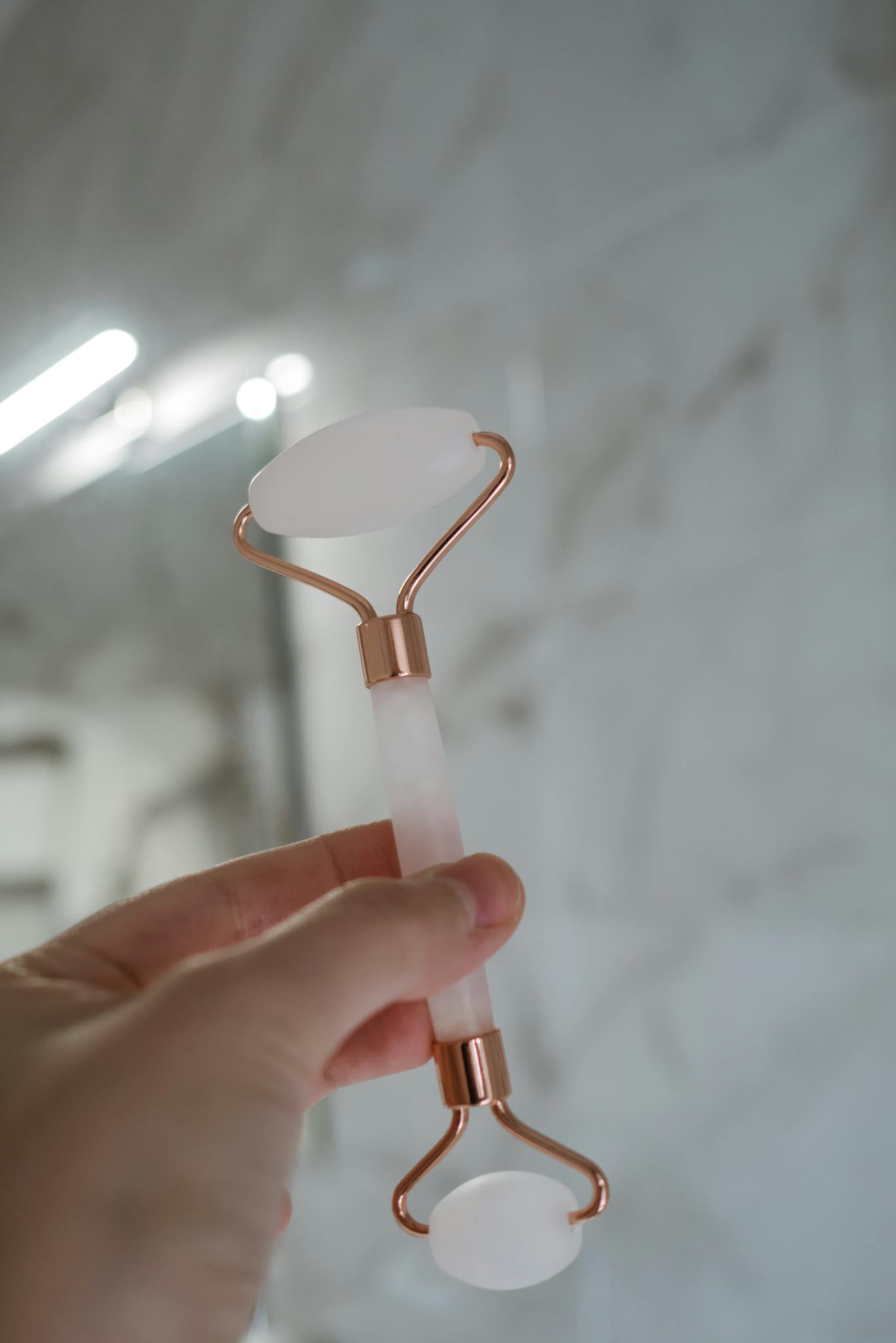 Close-up of a hand holding a rose quartz facial roller, ideal for skincare routines.