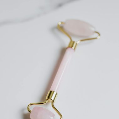 Elegant rose quartz facial roller for skincare on clean marble background.