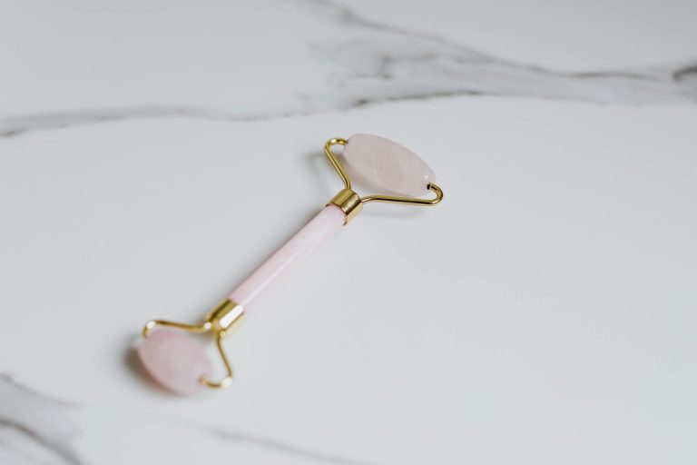Elegant rose quartz facial roller placed on a marble surface for beauty and skincare.