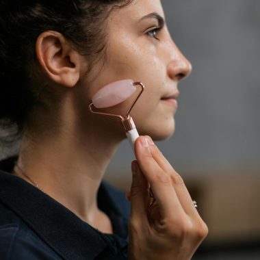 Side view of a woman massaging her face with a rose quartz roller in a beauty routine.