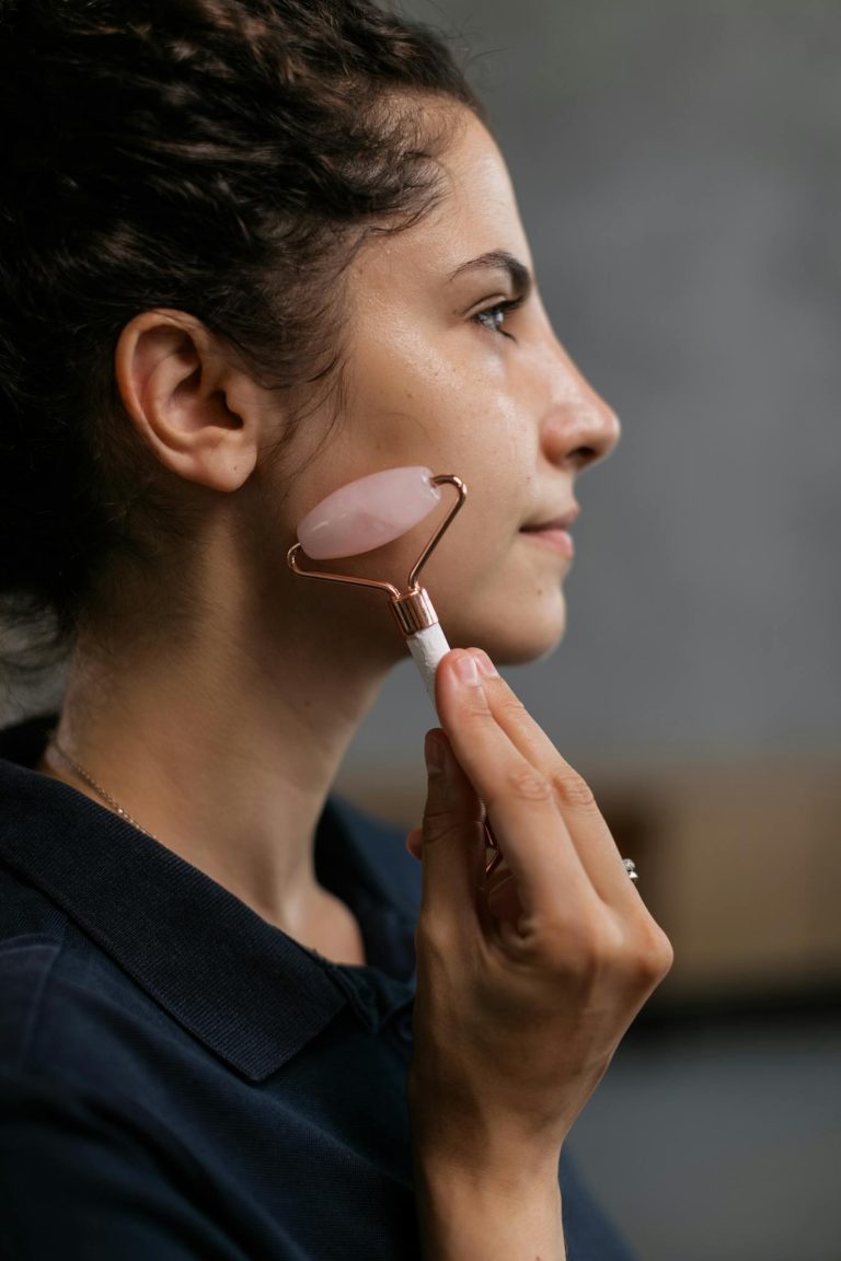 Side view of a woman massaging her face with a rose quartz roller in a beauty routine.