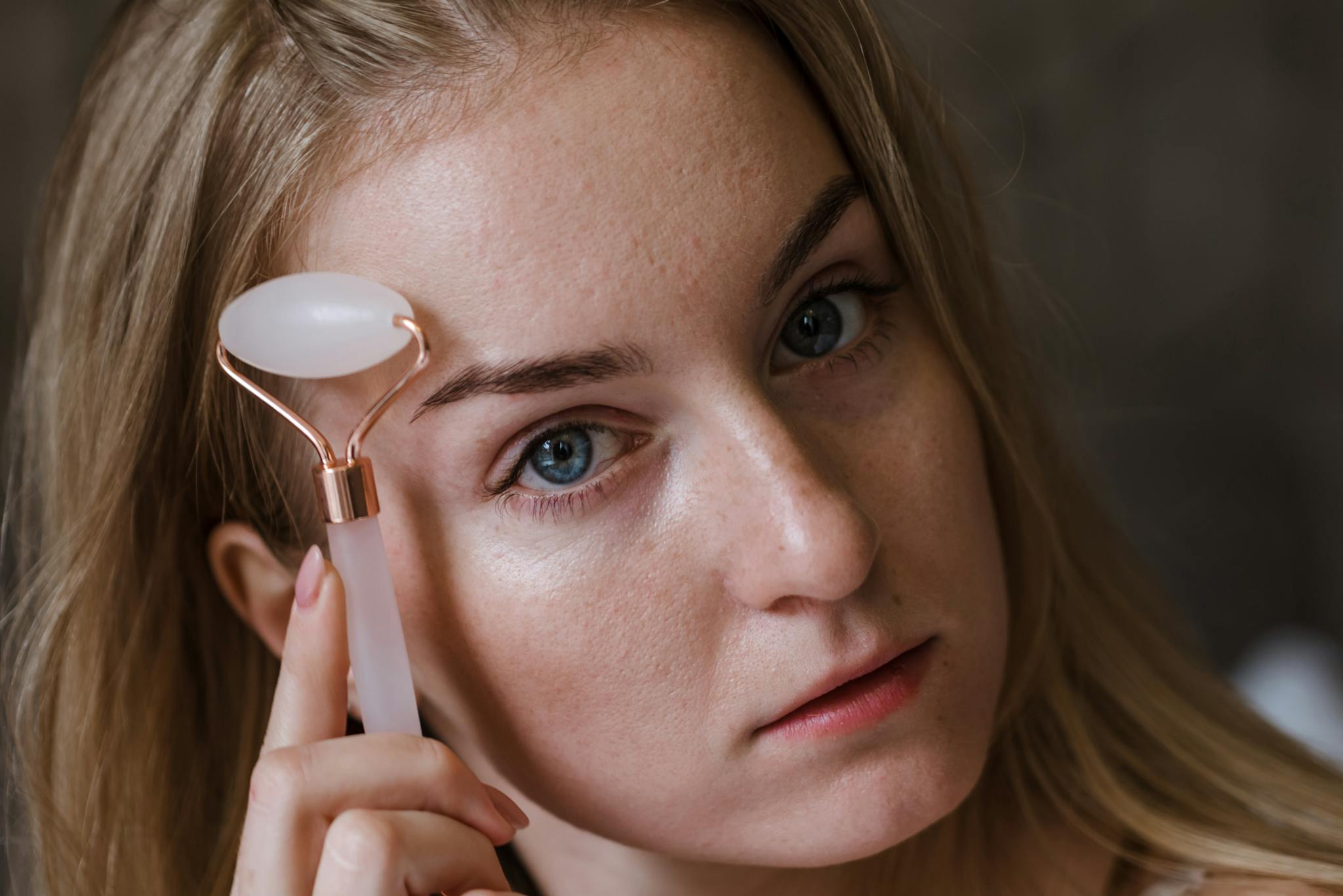 Young woman using a jade roller for facial massage, enhancing her skincare routine indoors.